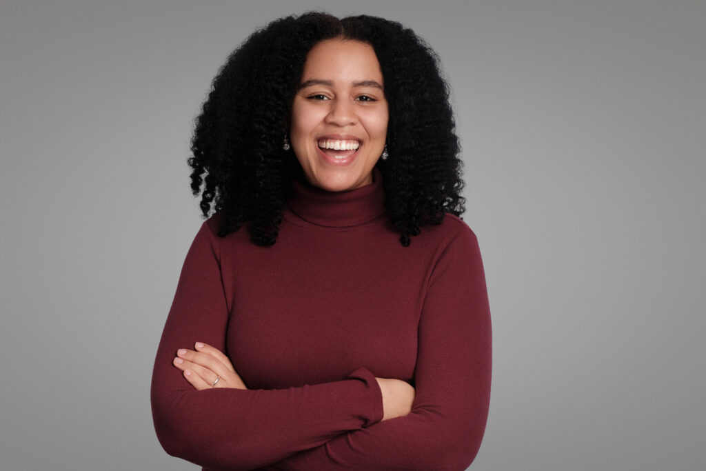 Woman with natural curls in burgundy turtleneck smiling, studio headshot in Boston